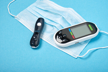 black blood glucose meter, lancet and face mask on blue background,