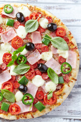 Pizza with ham, mozzarella cheese, cherry tomatoes, green and jalapeno pepper, black olives and fresh basil. Bright background. Top view. Close up.	