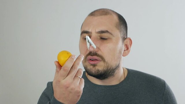 The man does not smell and taste, the sense of smell is lost, the symptoms of coronavirus. Man with a clothespin on his nose trying to smell the tangerine