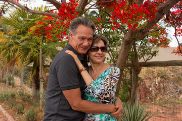 Happy mature couple embracing under a Red Formosa tree