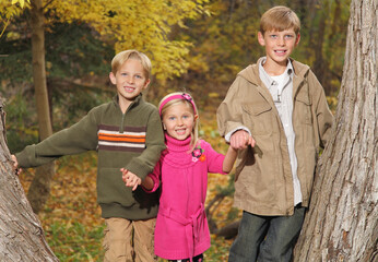three children holding hands together amongst the fall trees in autumn