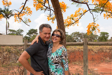 Happy mature couple embracing under a Yellow Formosa tree