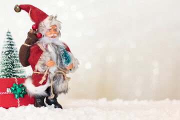 Santa Claus with christmas gift and christmas tree on snow. Blurred shiny background with copy space