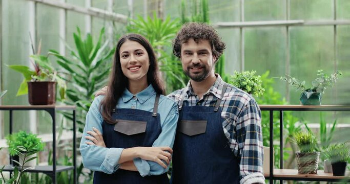 Portrait of happy man and woman in aprons standing at own small flower shop and smiling to camera after reopening. Caucasian cheerful couple entrepreneurs running own floral business. Store concept
