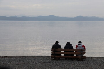 three people are sitting on a bench and looking into the distance against the background of the ocean