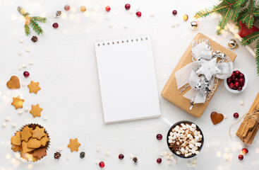 Fototapeta na wymiar Christmas gift box, empty notebook, cup of hot chocolate drink and homemade gingerbread cookies on white wooden background.
