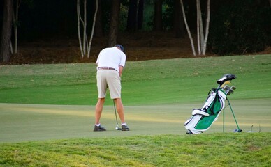 A senior elderly man putting on the green next to his bag on a hard and difficult luxury country club golf course.  