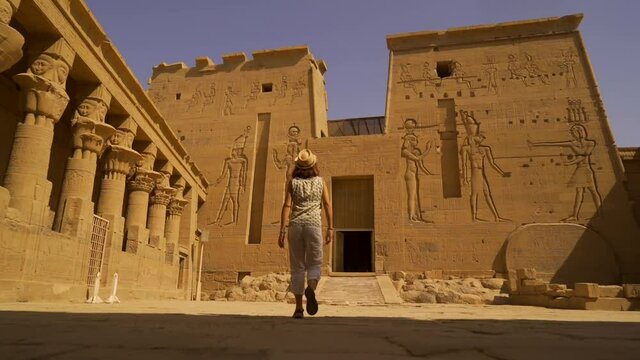 A young woman walking through the inner courtyard of the Temple of Philae, a Greco-Roman construction seen from the Nile River, a temple dedicated to Isis, the goddess of love. Aswan. Egyptian