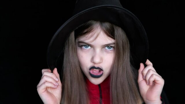 Emotional little / young girl in a witch hat sings a song on a dark background