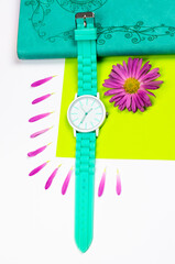 A mint-colored watch is on a notebook. Notepad and clock with flower petals