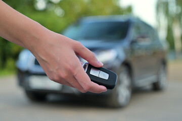 female hand holds out the car key against the background of a blurred car