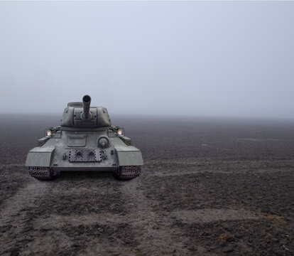 A tank approaching from fog on a muddy field on tracks