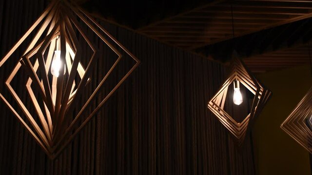 Defocus glowing light bulbs inside rhombus shape geometric lampshades. Night shot of modern wooden chandeliers with retro lamps in darkness - Powered by Adobe