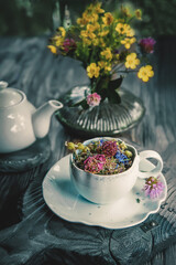 medicinal herbal tea with chamomile flowers and a bouquet of wild flowers in a beautiful Cup on a rustic wooden background. Rustic still life, authentic setting