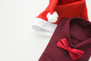 Bright red hat and man dark purple formal shirt with bow tie on white table background. Closeup. Garment for Christmas evening night. Empty place for text. Top down view.
