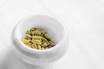 Raw organic cardamom pods are ready to use in a white stone mortar on a white background. Copy space
