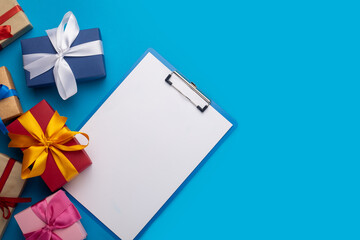 Clipboard with a blank sheet and gifts on a blue background. Gift shopping concept