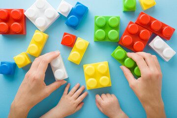 Young adult mother hands showing colorful plastic blocks to baby on light blue table background....