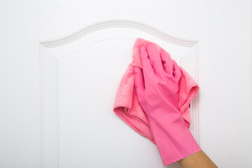 Woman hand in pink rubber protective glove wiping white wooden door with dry rag. General or regular cleanup. Cleaning service. Closeup.