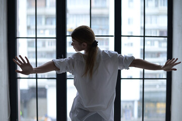 woman yawns in front of a window overlooking the city in the morning