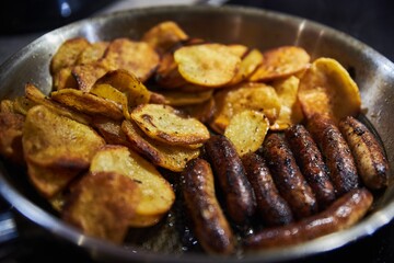 Bratwurst and chips in a pan. German brat and fried potatoes in a pan. Making brats and home fries.