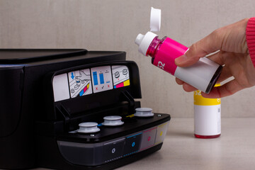 a woman's hand pours paint from a bottle into the printer