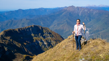 Naklejka na ściany i meble Woman hiker goes hiking, stands on top of mountain and looks at autumn nature mountains landscape in sunny weather. Outdoor activities. Copy space