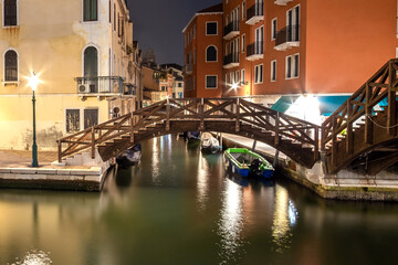 Fototapeta na wymiar Night view of illuminated old architecture, floating boats and light reflections in canals water in Venice, Italy.