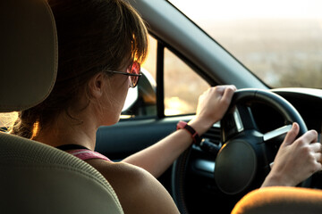 Fototapeta premium Close up view of a woman driver holding steering wheel driving a car at sunset.