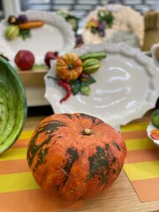 An orange and green pumpkin lies on the table against the background of decorative plates with the image of vegetables.