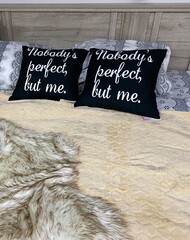 Black two black pillows with white lettering Nobody is perfect except me lie on the bed linen in pastel colors.