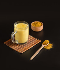 Glass Cup with healthy Indian drink Golden milk-turmeric latte mixed with cardamom, ginger, cinnamon, allspice on black background. Vertical frame