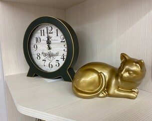 Composition with a Golden cat figurine and vintage clock standing on the shelf of the Cabinet.