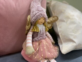 A small plush doll with Golden wings and a fur hat sits half-turned among pink and white pillows.