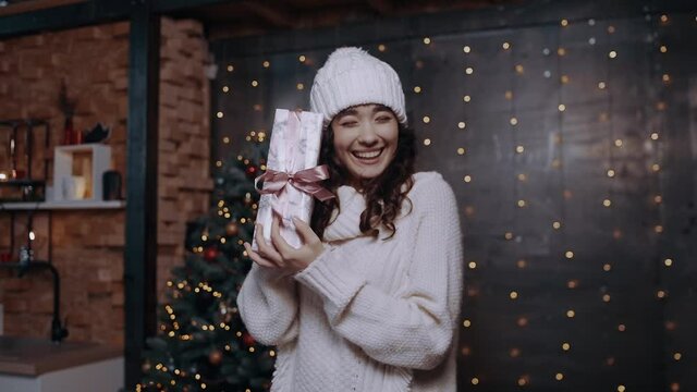 Beautiful teenager with a wide smile. The young woman with the white hat and thick clothes inside who holds a gift in her hand and is happy. Holiday concept. New Year 2020