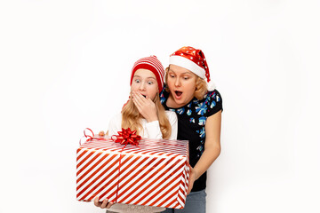 Shocked, surprised and happy mom and daughter in Santa hats, holding a big Christmas present in their hands on a white background. Photo with copy space for text