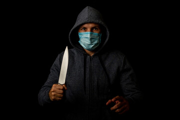 Young man in medical mask points finger while holding knife on black background.