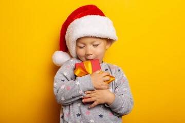 Child in a Christmas hat holds a gift on a yellow background. Gifts for Christmas, Christmas morning