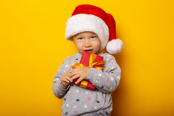 Child in a Christmas hat holds a gift on a yellow background. Gifts for Christmas, Christmas morning