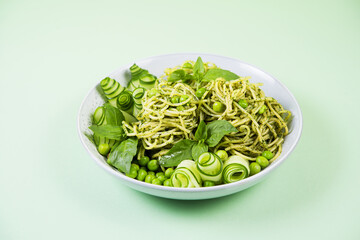Spaghetti with green pesto sauce, garnished with fresh cucumber and green pea