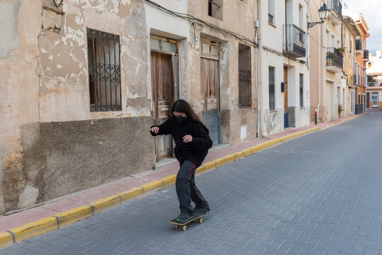 Girl rides a skateboard in a village wearing a protective face mask.