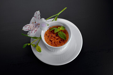 Dessert creme brulee, in a white dish with mint leaves in white flowers, on a dark background, with a place for text