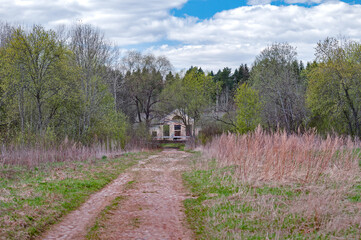 An old, cobblestone, grassy road leading to the train station, with an abandoned station building