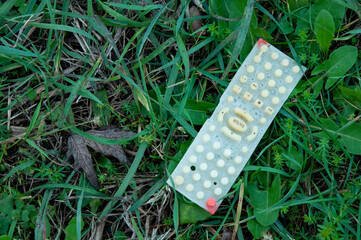 the TV remote control lies on wet grass on a cloudy day and you can see rain drops on it
