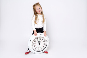 The girl stands and holds a large white clock near her feet. Isolated over white background.