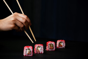 Female hand takes chopsticks california sushi rolls with Chinese chopsticks. Selective focus, black background