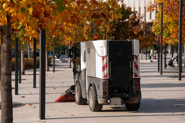 A swiper sweeps autumn leaves in a park square.