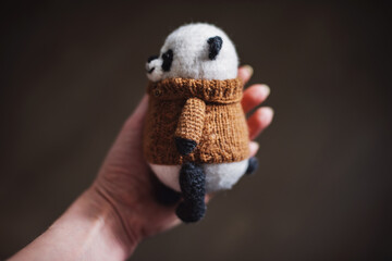Handmade knitted toy. Amigurumi panda toy in camel color sweater on the wooden  background. Crochet...