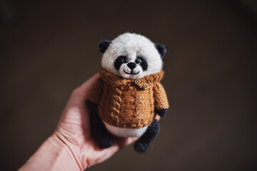 Handmade knitted toy. Amigurumi panda toy in camel color sweater on the wooden  background. Crochet stuffed animals.One of the three sides. front of