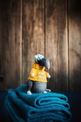Fototapeta premium Handmade knitted toy. Amigurumi black rat toy in blue hat and yellow sweater on the blue and wooden background . Crochet stuffed animals.